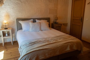 Ein Schlafzimmer mit einem Bett, einem Nachttisch mit Lampe, Holzboden und Steinwand.