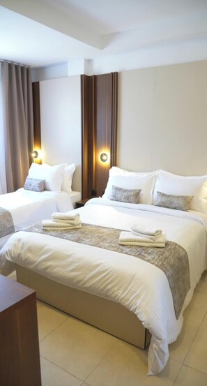 A hotel room with two beds, a wooden headboard, a nightstand, and a view of the city. - Cozzy Inn (Oran)