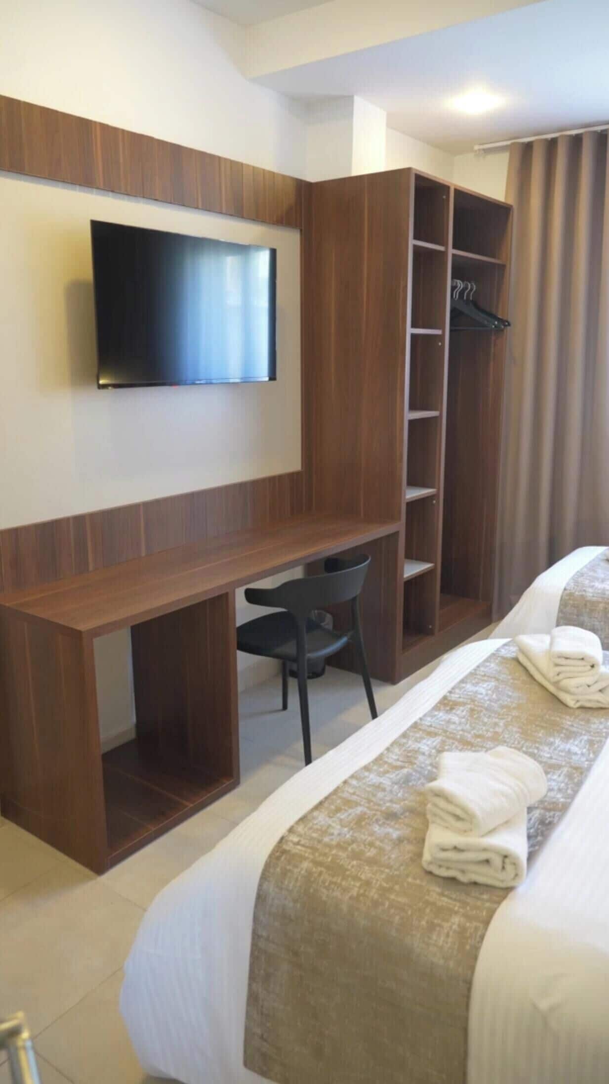 Habitación de hotel con cama, escritorio, silla, televisor y armario.