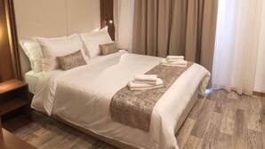 A hotel room with a large bed, a wooden floor, a nightstand, and a window with curtains. - Cozzy Inn (Oran)