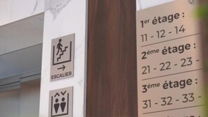 A wall with emergency exit signs and a list of room numbers by floor. - Cozzy Inn (Oran)