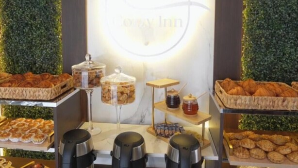 A buffet setup with a central logo, various food items, and coffee dispensers. - Cozzy Inn (Oran)