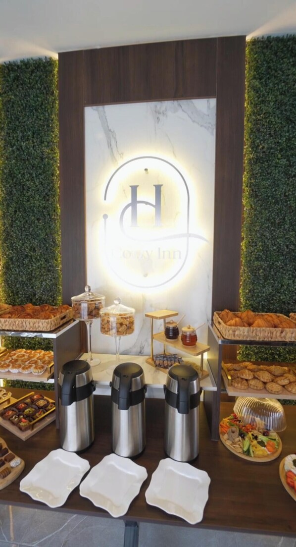 A buffet setup with a central logo, various food items, and coffee dispensers. - Cozzy Inn (Oran)
