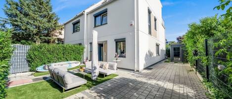 A modern two-story house with a patio, a swimming pool, and a fenced garden area.