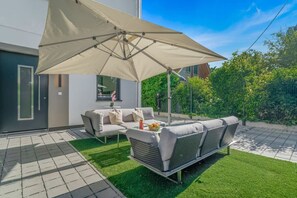 An outdoor seating area with a sofa and chairs, a table with fruit, and a large umbrella. - Modern Luxury Villa, 5 Bedrooms, Alte Donau (Wien)