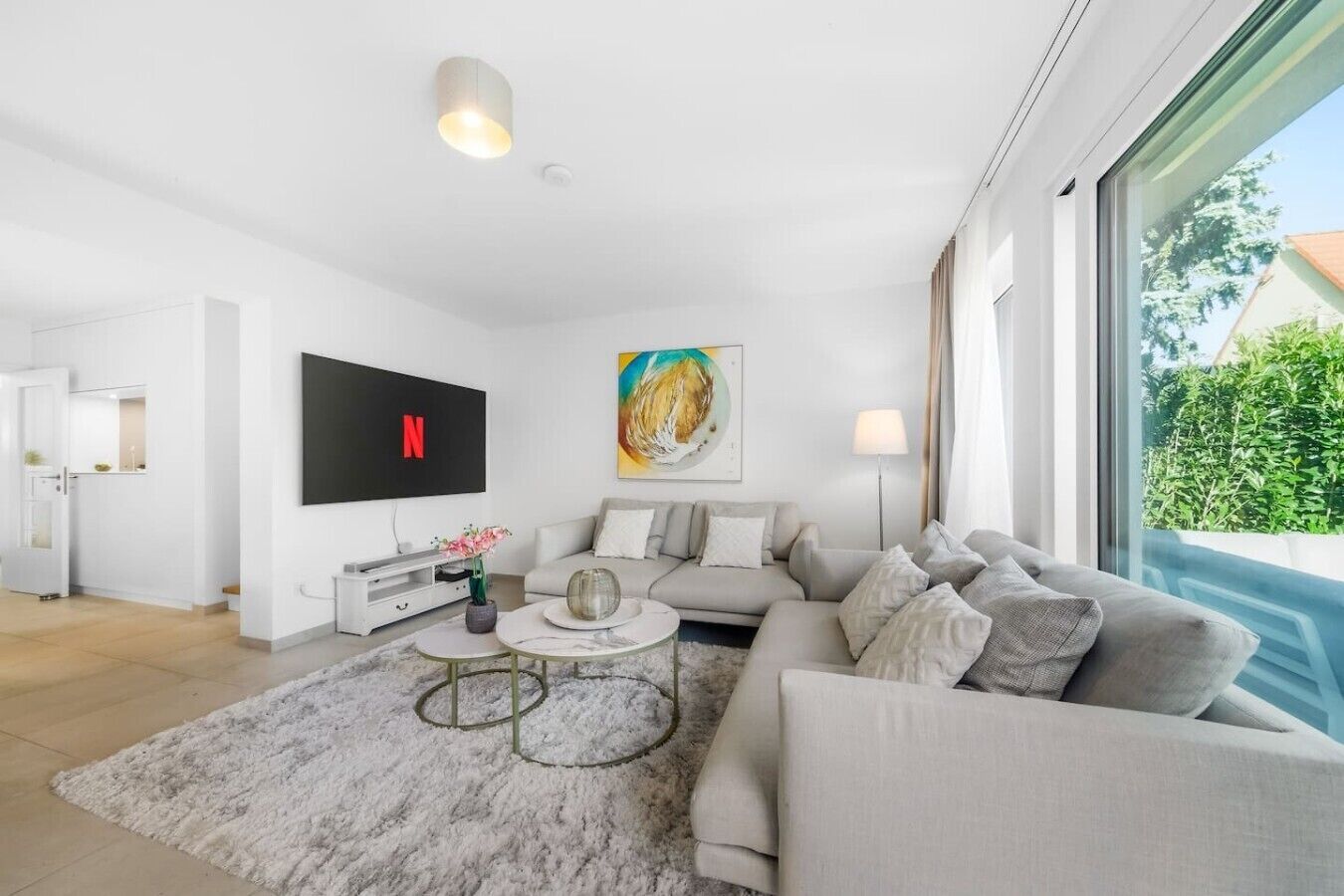 Ein modernes Wohnzimmer mit grauem Sofa, einem Flachbildfernseher, einem Couchtisch und einem Gemälde an der Wand.
