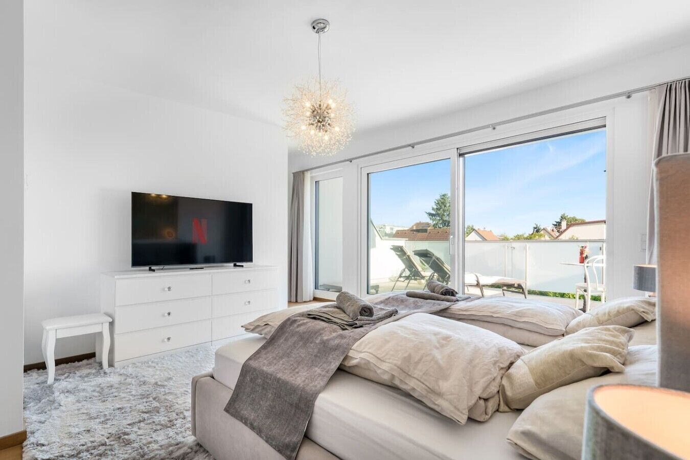 Ein Schlafzimmer mit Fernseher, Bett, kleinem weißen Tisch und großem Fenster.