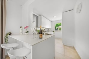 Eine moderne Küche mit Kochinsel, Barhocker, einer Weinflasche und einem Blumentopf.