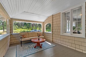 Eine überdachte Veranda mit einem Holztisch, einer gepolsterten Bank und einem Fahrzeug im Hintergrund.