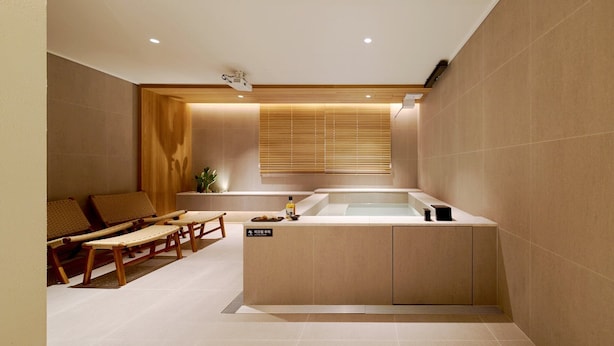 A spa room with a bathtub, wooden seating, and a small table with amenities. - Anook Hotel Busan Gwangalli (Busan)