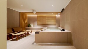 Une salle de spa équipée d’une baignoire, de sièges en bois et d’une petite table avec des accessoires.