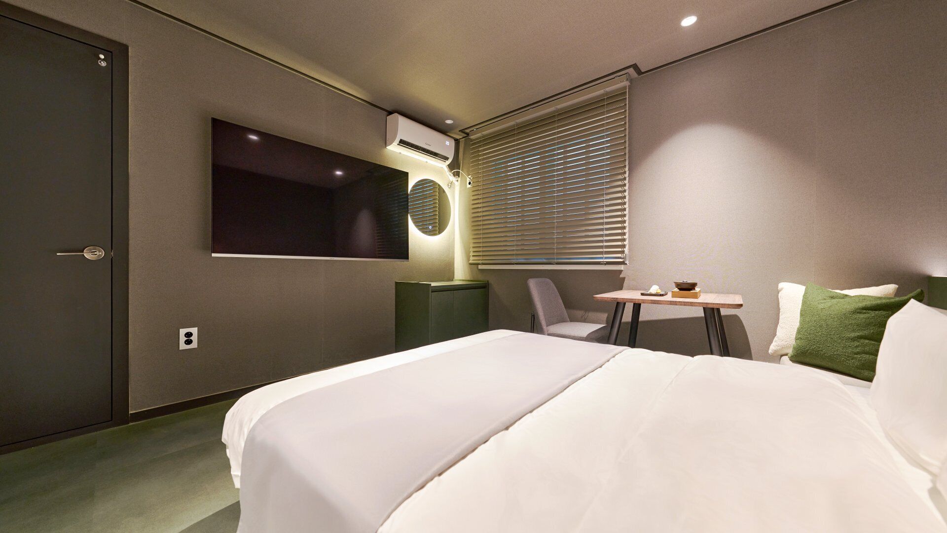 Habitación de hotel con cama, escritorio, silla, televisor y aire acondicionado.