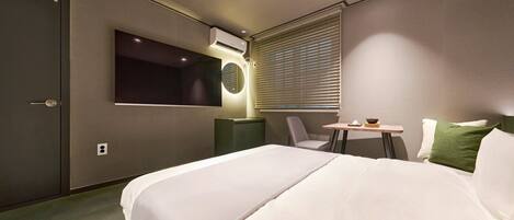 Habitación de hotel con cama, escritorio, silla, televisor y aire acondicionado.