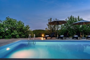 Ein Swimmingpool mit Liegestühlen und Sonnenschirmen, umgeben von viel Grün.