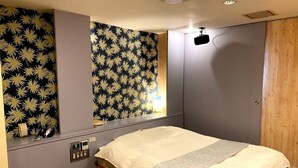 Un dormitorio con cama, mesita de noche, espejo y pared con estampado floral.