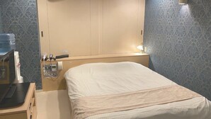 Habitación de hotel con cama, mesita de noche y lámpara de pared.