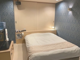 Habitación de hotel con cama, mesita de noche y lámpara de pared.