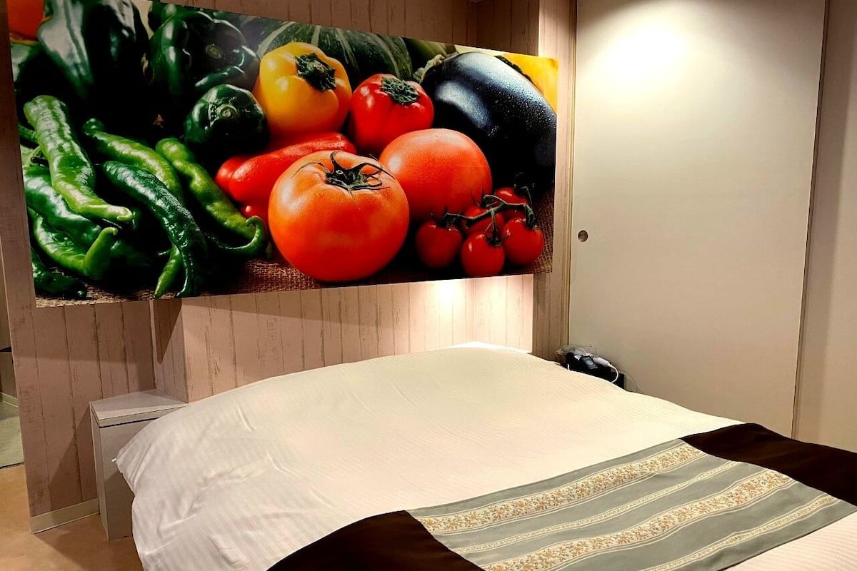 Un dormitorio con cama, mesita de noche y televisor de pared mostrando verduras.