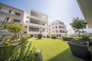 Un bâtiment moderne doté de nombreux balcons et d’une cour bien entretenue, avec une pelouse artificielle et des plantes en pot.