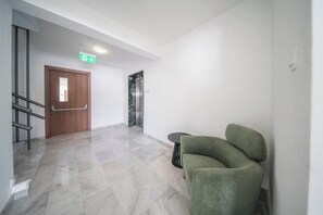 A hallway with a wooden door, a green cushioned chair, and a marble floor. - Serene Gardens 2BR w/ Pool (Livadia Larnakas)