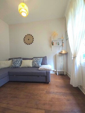 Una sala de estar con sofá, decoración en la pared, radiador y estantería.