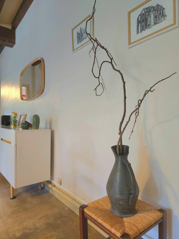 A room with a white cabinet, a mirror, a vase with branches, and framed pictures on the wall.