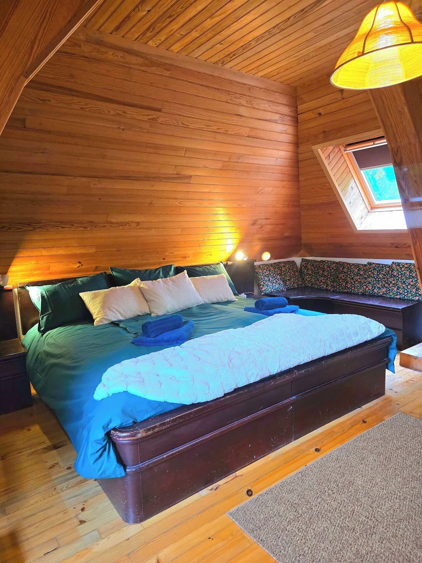 A wooden-paneled room with a bed, a bench, and a skylight.
