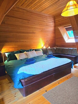 A wooden-paneled room with a bed, a bench, and a skylight.