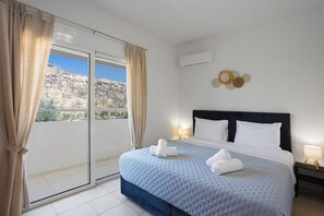 A hotel room with a bed, a view of a mountainous landscape, and a wall-mounted air conditioning unit.