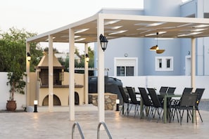 Un patio exterior con zona de estar techada, una parrilla y una piscina.