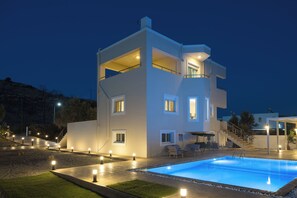 Una casa moderna de dos pisos con piscina, mobiliario exterior y fachada bien iluminada.