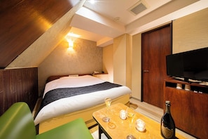 Habitación de hotel con una cama, televisión, una mesa con vasos y una botella, y una silla verde.