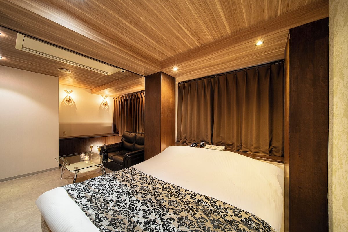 A modern hotel room with a large bed, a seating area with a glass table, and a wall-mounted TV.