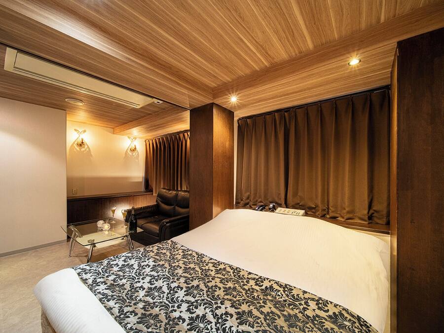 A modern hotel room with a large bed, a seating area with a glass table, and a wall-mounted TV.