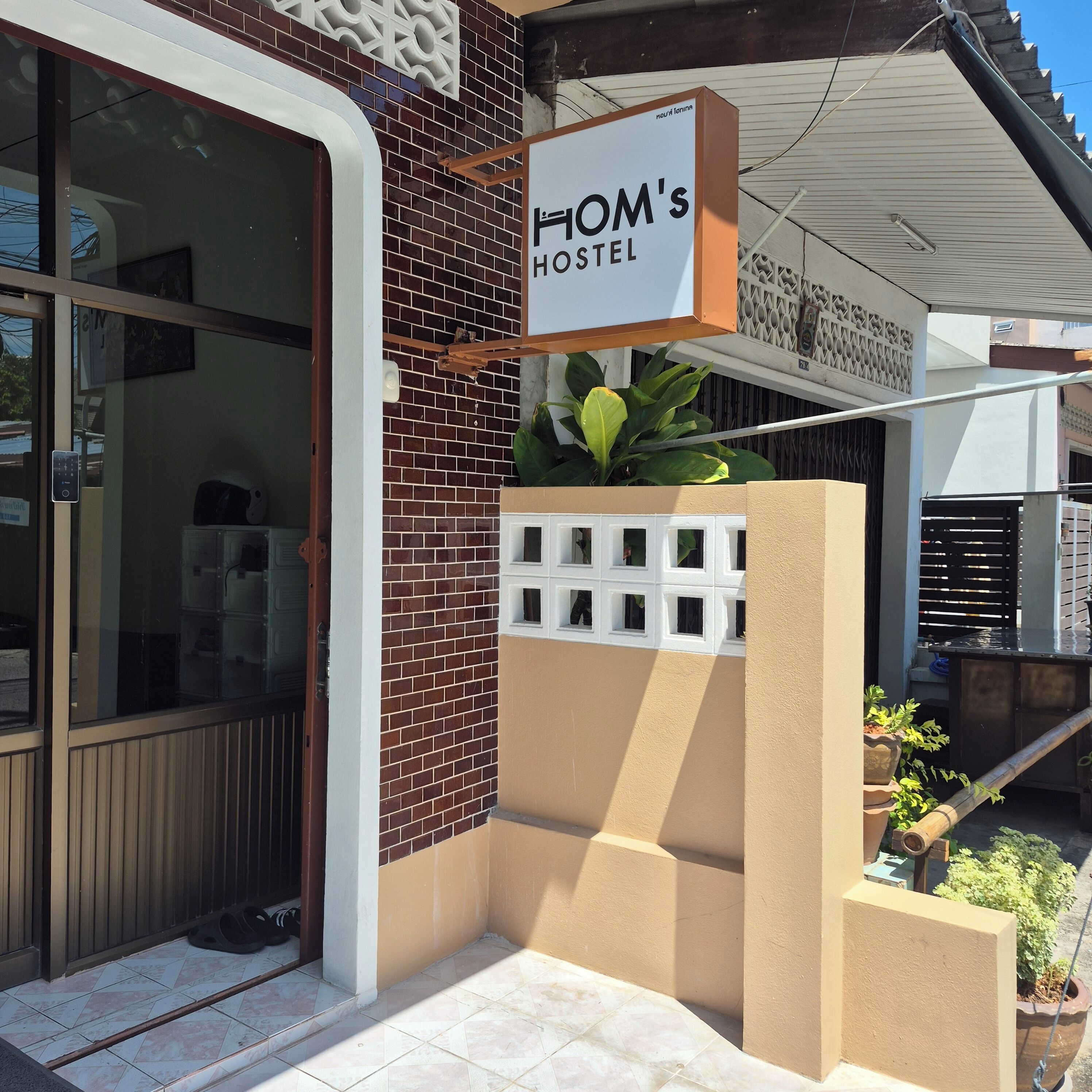 A hostel entrance with a sign reading 'HOM's HOSTEL', a brick wall, and a gated entrance.