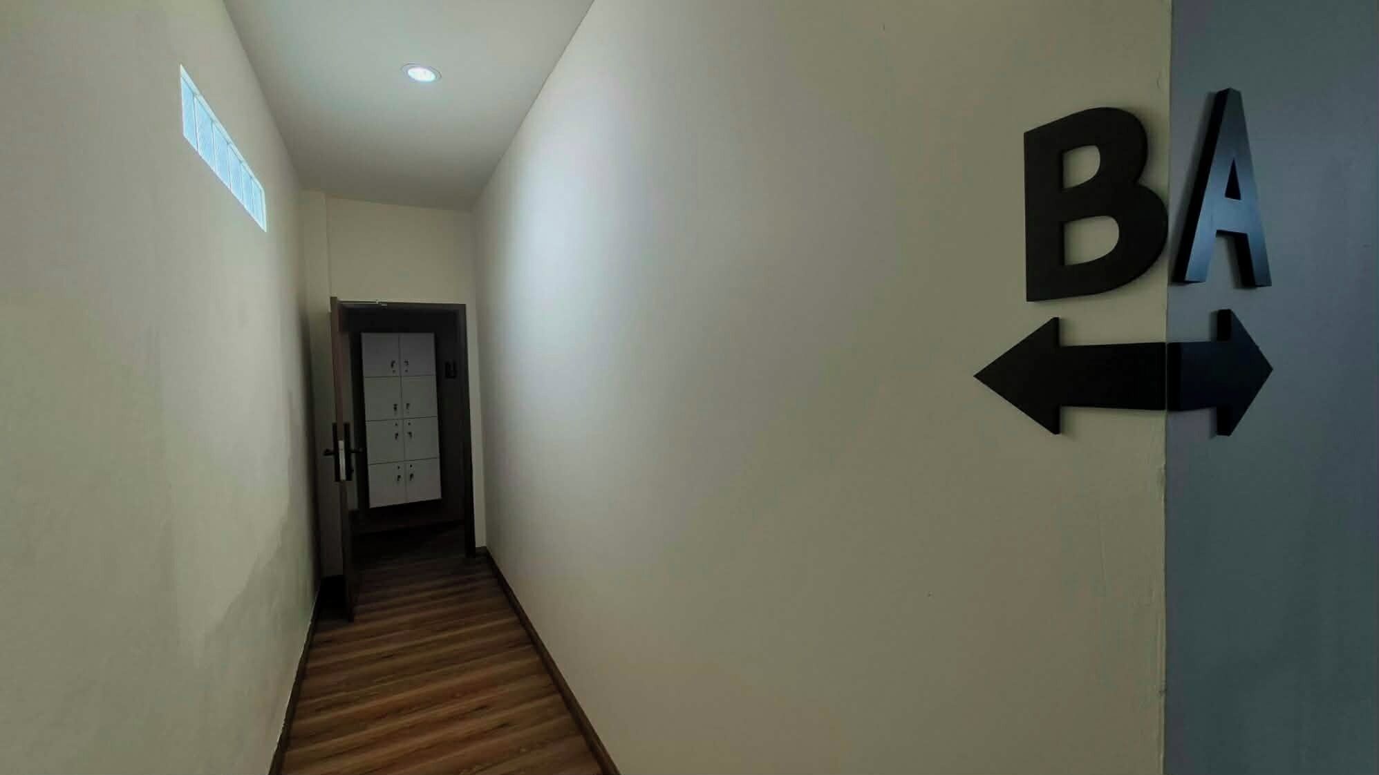 Un pasillo con suelo de madera, una puerta al final y señalización en la pared.