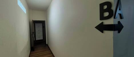 A hallway with a wooden floor, a door at the end, and directional signs on the wall.
