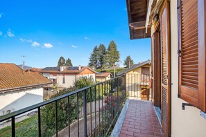 Ein Wohnbalkon mit Metallgeländer, einem Backsteinweg und Blick auf Nachbarhäuser und Bäume.