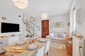 A modern kitchen with a dining area, a TV mounted on the wall, and a staircase leading to an upper level. - Alba Rosa Apartment - 2 Bed, 2 Bath (Taino)