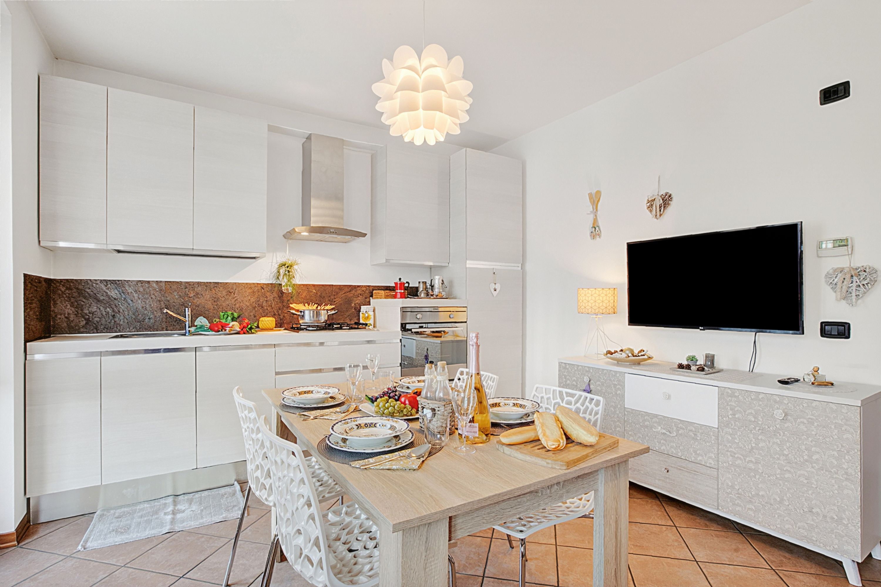 Una cucina moderna con mobili bianchi, un tavolo da pranzo per quattro persone e un televisore a schermo piatto montato a parete.