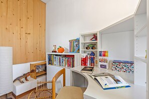 Ein Zimmer mit einer Holzwand, einem weißen Schreibtisch mit Stuhl, Bücherregalen und verschiedenen Spielsachen.