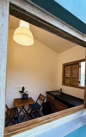 Uma cozinha compacta com mesa de madeira, cadeiras, luminária pendente, janela com persianas e pia.