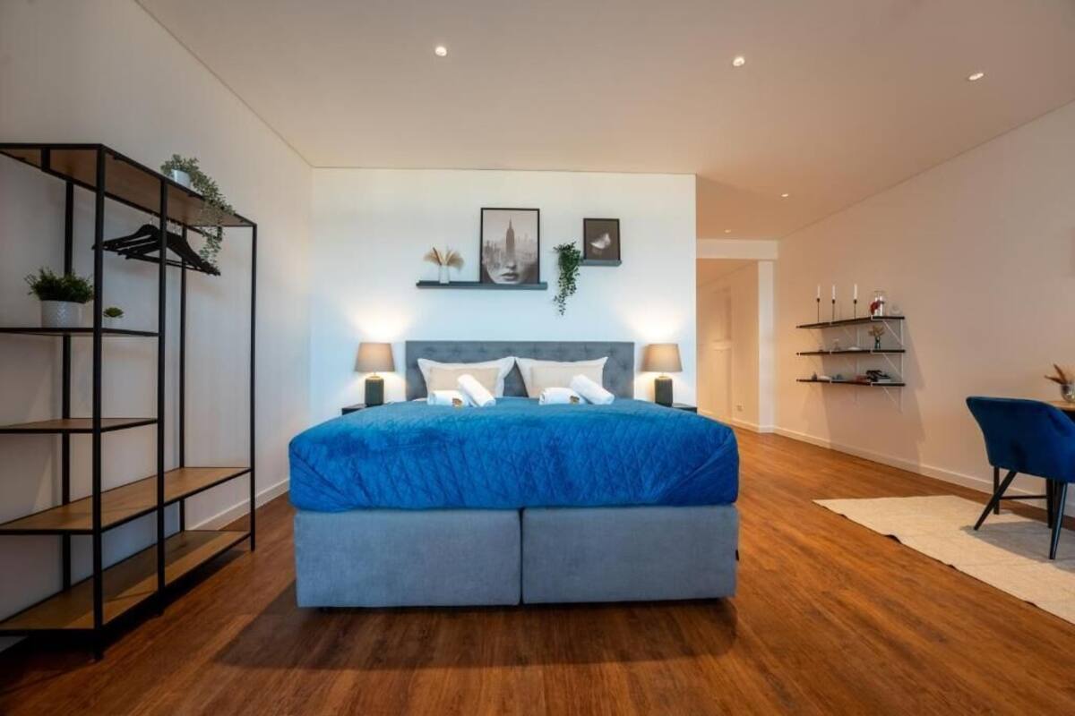 A modern bedroom with a large bed, bedside lamps, a bookshelf, and a desk with a chair.
