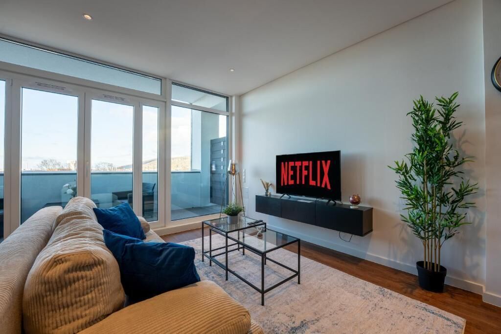 A modern living room with a large window, a sofa, a coffee table, a TV on a black stand, and a potted plant.