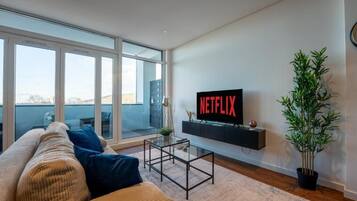 A modern living room with a large window, a sofa, a coffee table, a TV on a black stand, and a potted plant.
