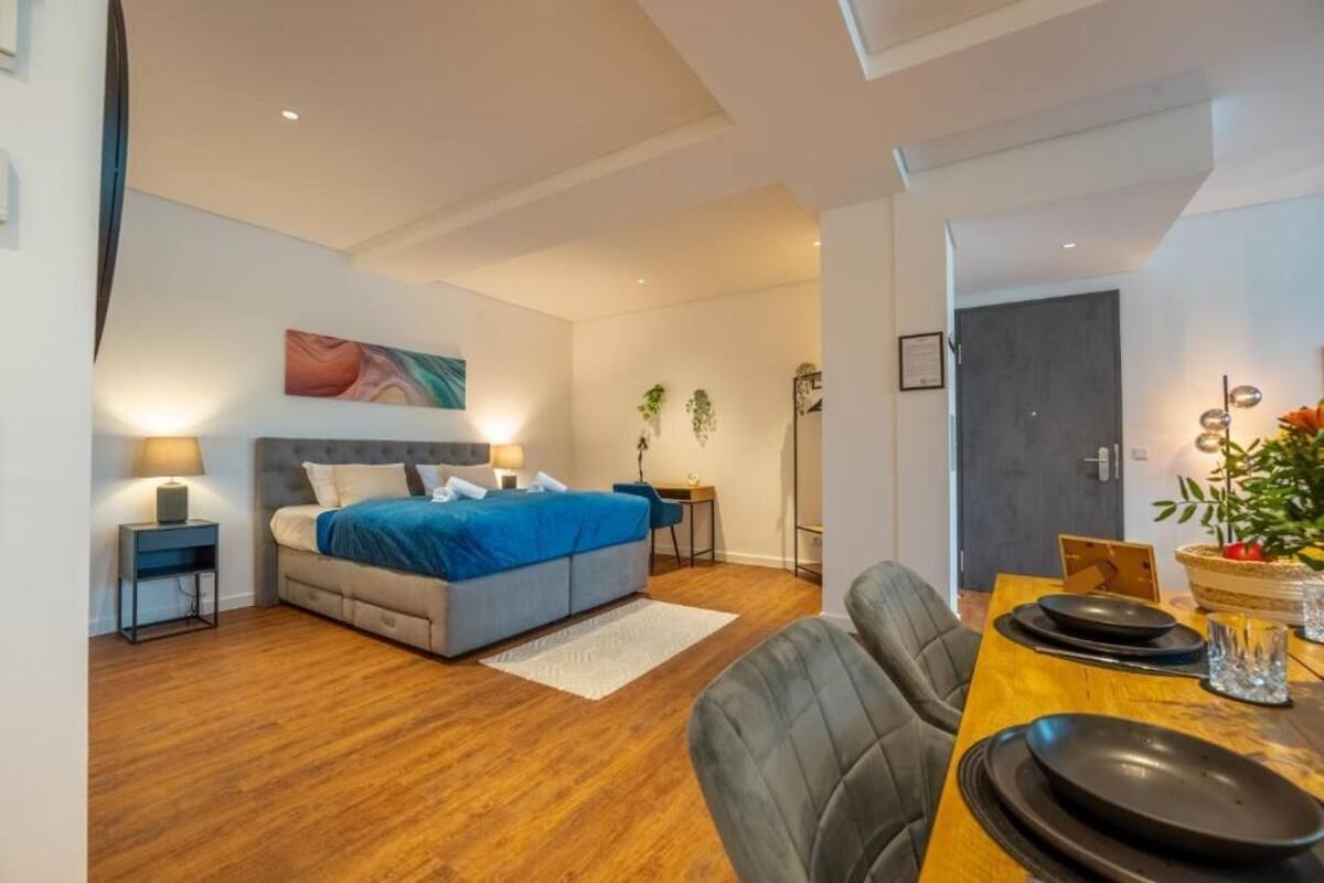 A modern bedroom with a bed, bedside tables, a desk, and a dining area with chairs and a table.