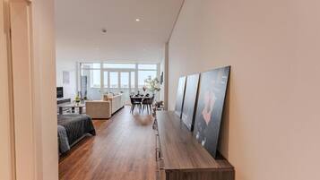 A modern interior with a long wooden bench, a dining area with a table and chairs, and a large window providing natural light.