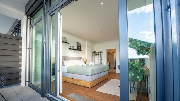 Un dormitorio moderno con una cama grande, un ventanal corredero que da a un balcón y vistas al cielo.