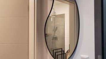 A bathroom with a large mirror, a shower, and a door.