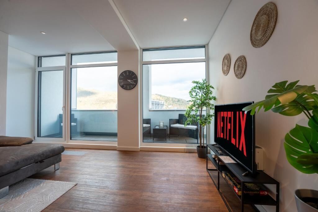 Een moderne woonkamer met een groot raam, een bank, een televisie en een potplant.